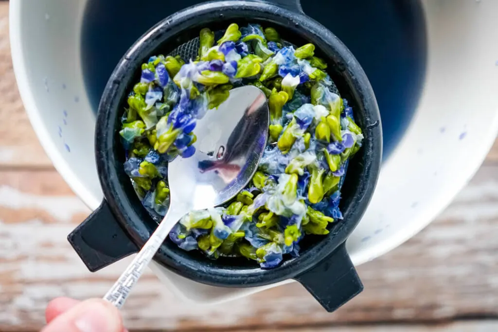 A spoon pressing the liquid from the steeped violet flowers. 